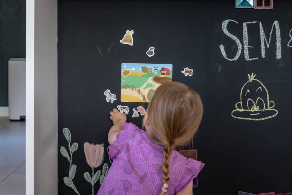 Kind legt magnetische Spielfiguren an eine schwarze magnetische Tafelwand