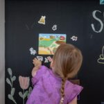 Kind legt magnetische Spielfiguren an eine schwarze magnetische Tafelwand
