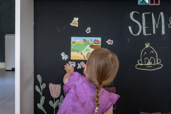Kind legt Magnete an die Tafelwand Kind legt magnetische Spielfiguren an eine schwarze magnetische Tafelwand