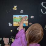 Kind legt magnetische Spielfiguren auf ein Magnetspielbrett an einer magnetischen Tafelwand