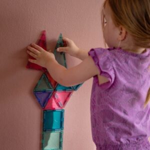 Kind baut mit magnetischen Bausteinen an einer rosa gestrichenen Wand mit MagnetFarbe darunter