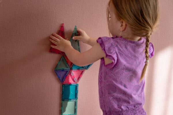 Magnetische Wand im Kinderzimmer Kind baut mit magnetischen Bausteinen an einer rosa gestrichenen Wand mit MagnetFarbe darunter