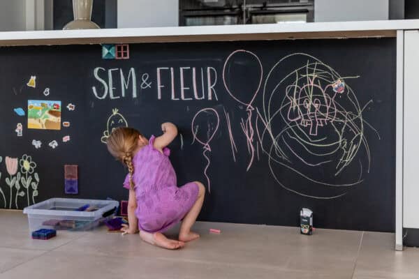 Kind malt mit Kreide an der Tafelwand Kind malt mit Kreide an einer mit SchultafelFarbe gestrichenen Wand