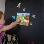 Mädchen spielt mit den Magneten Mein kleiner Bauernhof an einer schwarzen Magnetwand