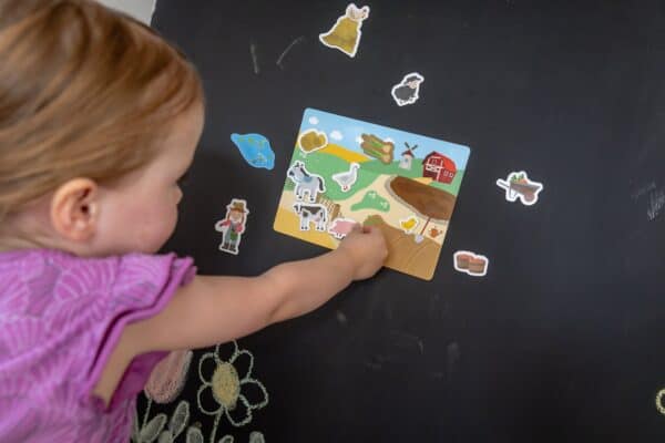 Bauernhof-Magnete Spielbrett mit Pferd, Kuh und Schwein Kind setzt ein Schwein auf das Bauernhof-Spielbrett mit Pferd, Kuh und Küken