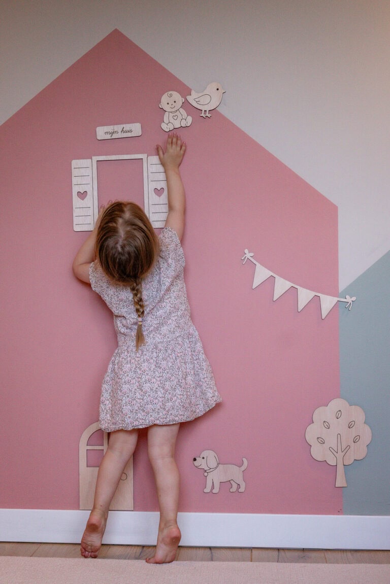 Mädchen spielt mit magnetischen Holzfiguren an einer mit MagnetFarbe gestrichenen Hauswand im Kinderzimmer
