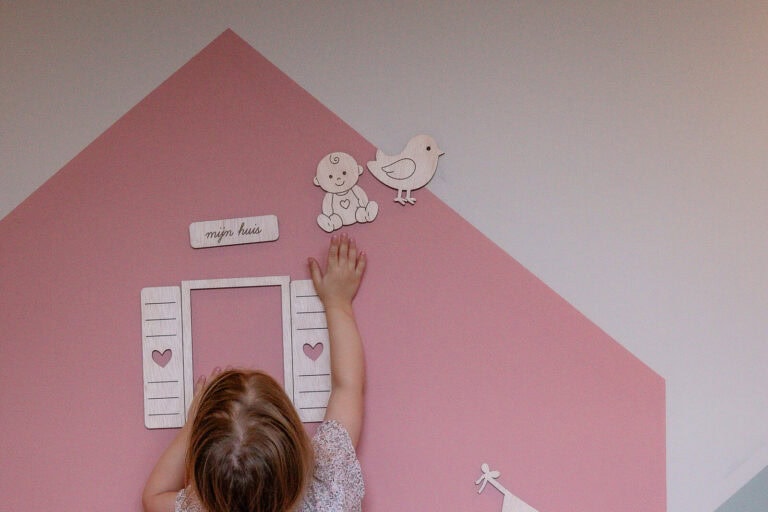 Mädchen spielt mit magnetischen Holzfiguren an einer mit MagnetFarbe gestrichenen Hauswand im Kinderzimmer